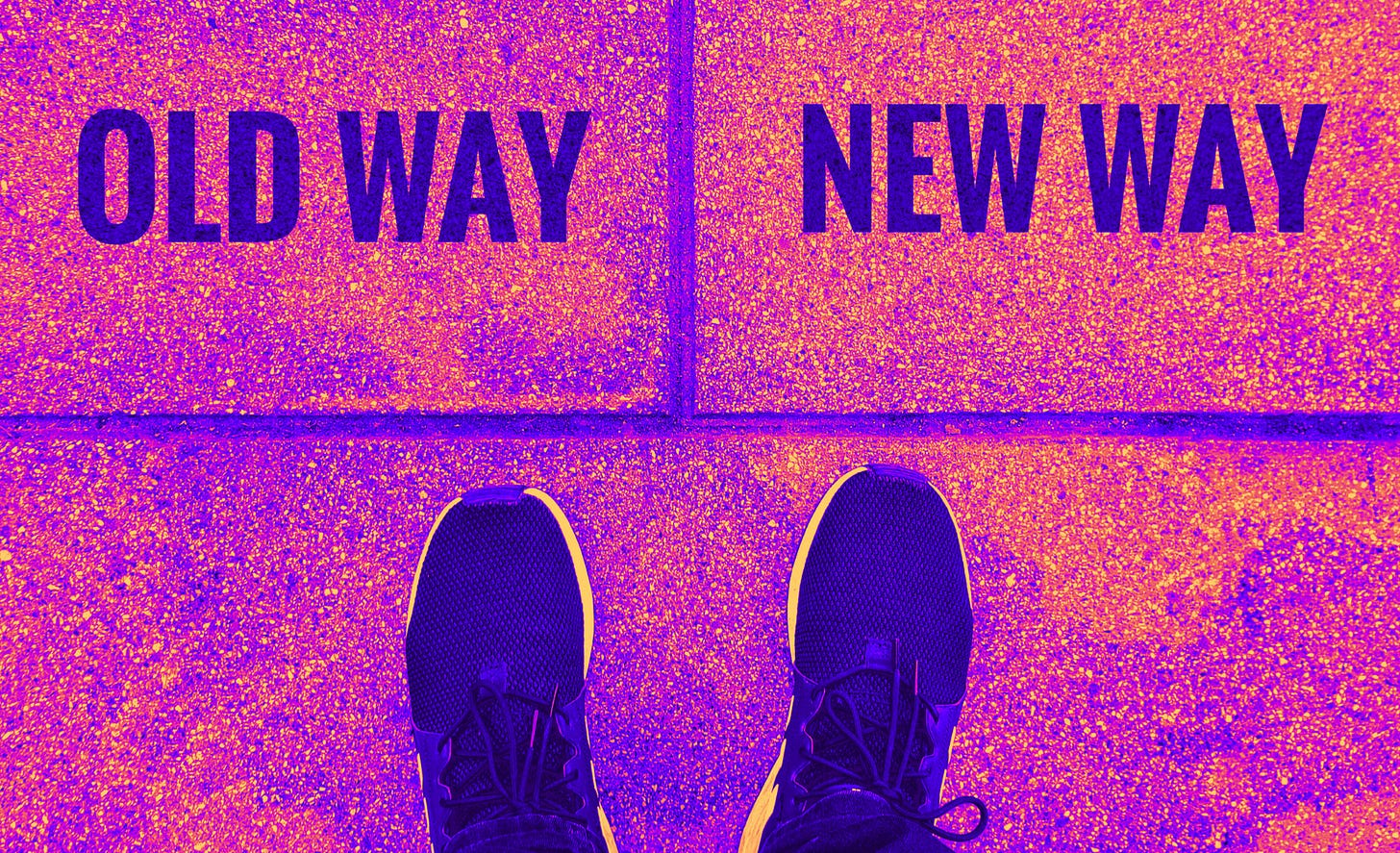 A pair of feet in sneakers stands at a crossroads where two sidewalk tiles are labeled "OLD WAY" on the left and "NEW WAY" on the right. The image is heavily color-edited in vibrant purples, oranges, and yellows, creating a high-contrast, surreal effect. The person appears to be facing the choice between the old path and a new direction.