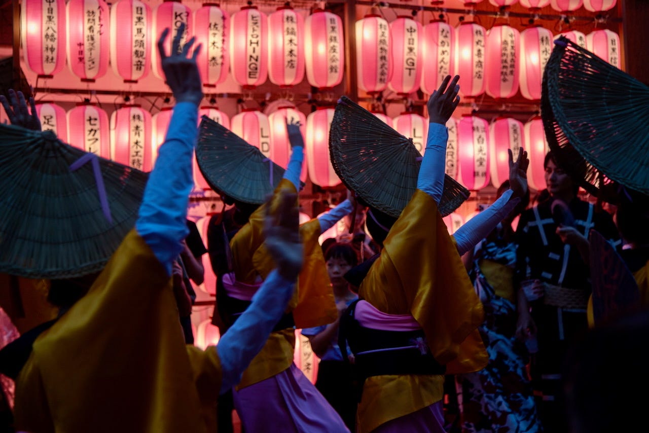 Dancers in yellow and purple yukata raise their hands beneath rows of glowing pink paper lanterns at the Nakameguro Summer Festival in Tokyo. Dancers in yellow and purple yukata raise their hands beneath rows of glowing pink paper lanterns at the Nakameguro Summer Festival in Tokyo.
