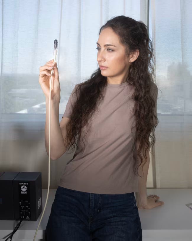 Kate standing in a room holding a wire with a small rounded tip on the end