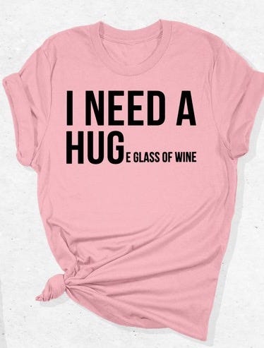 May include: A pink t-shirt with the text 'I need a hug and a glass of wine' in black text.