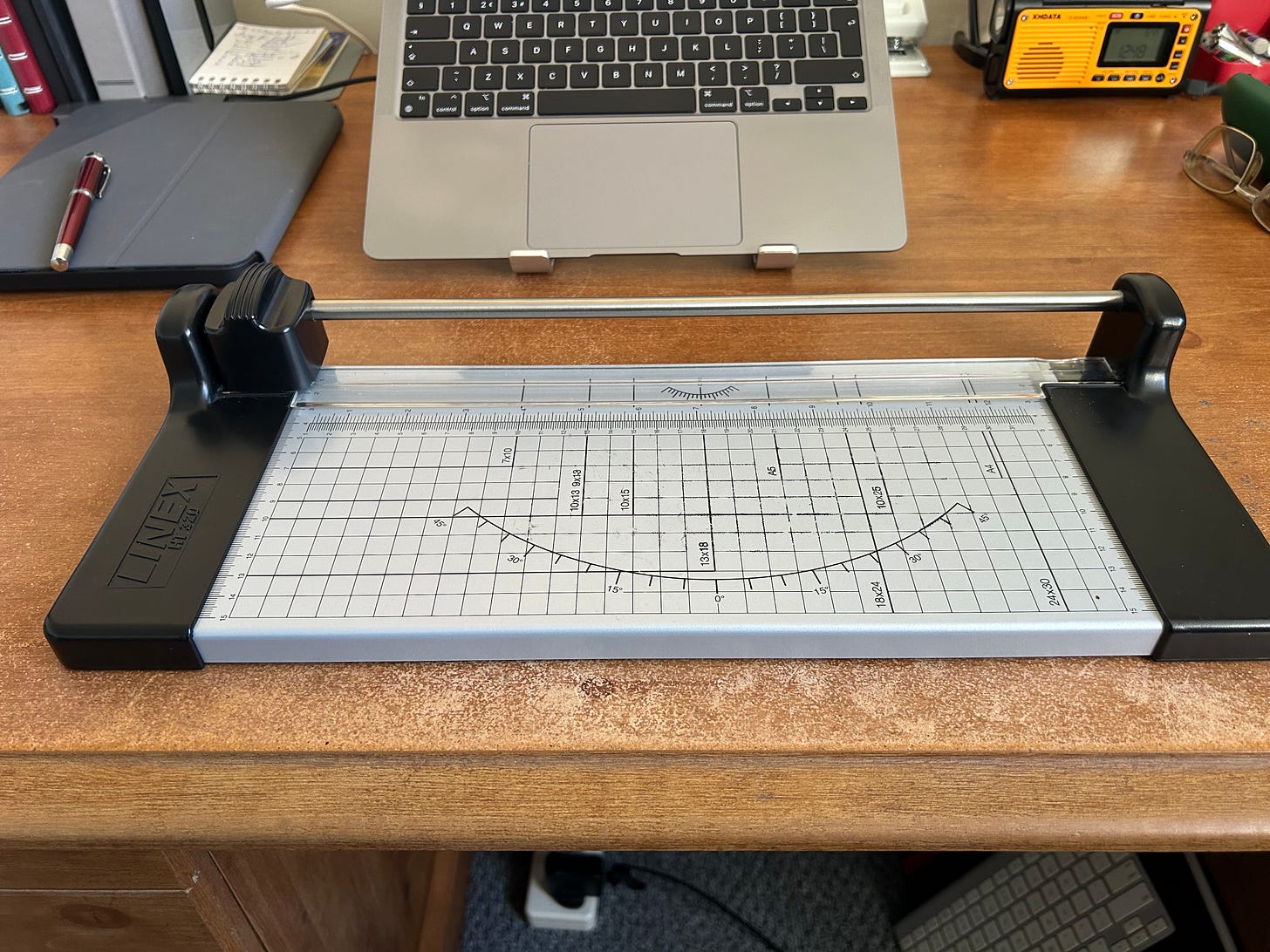A paper cutter sitting on desk with a laptop in the background.