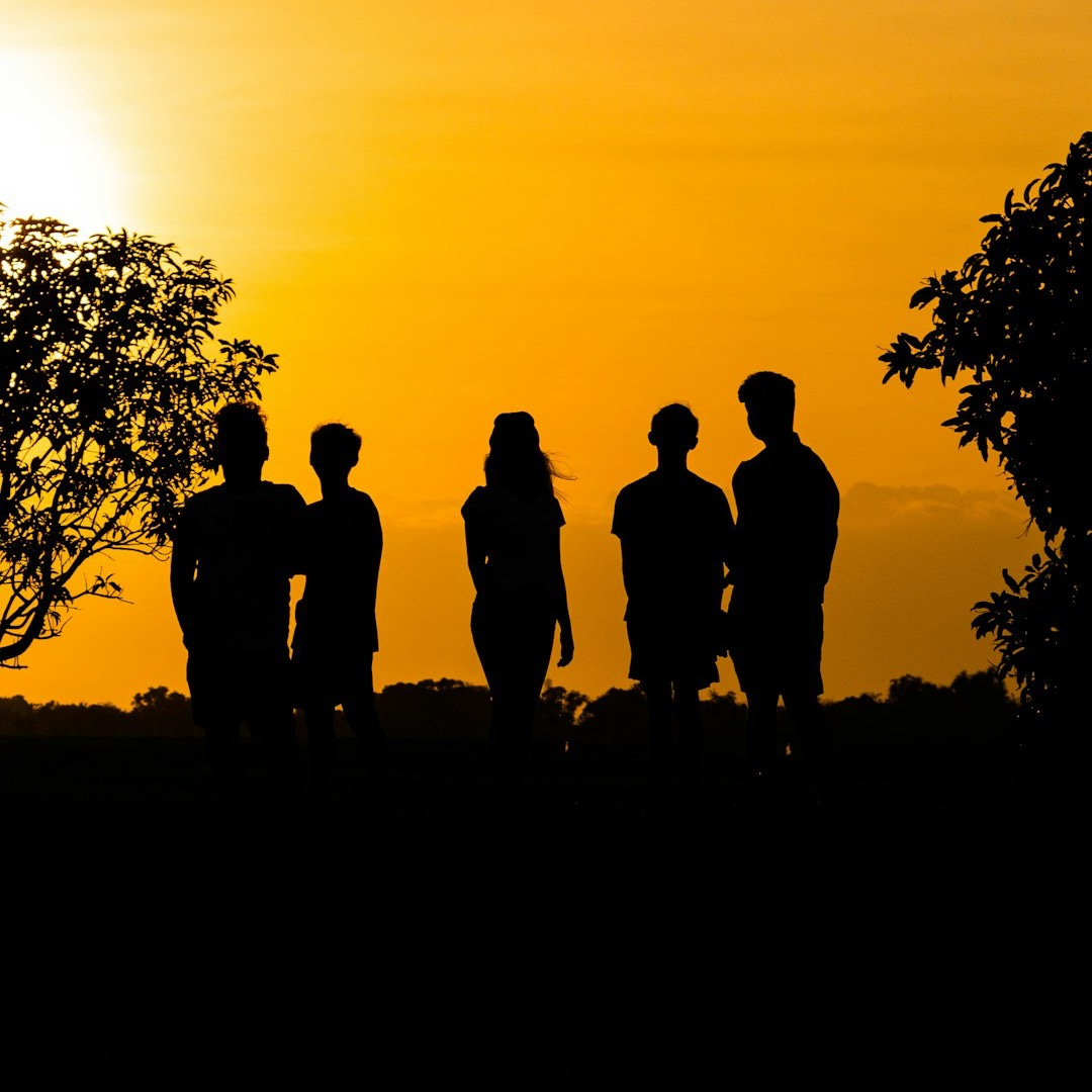 silhouette of 3 men standing near tree during sunset