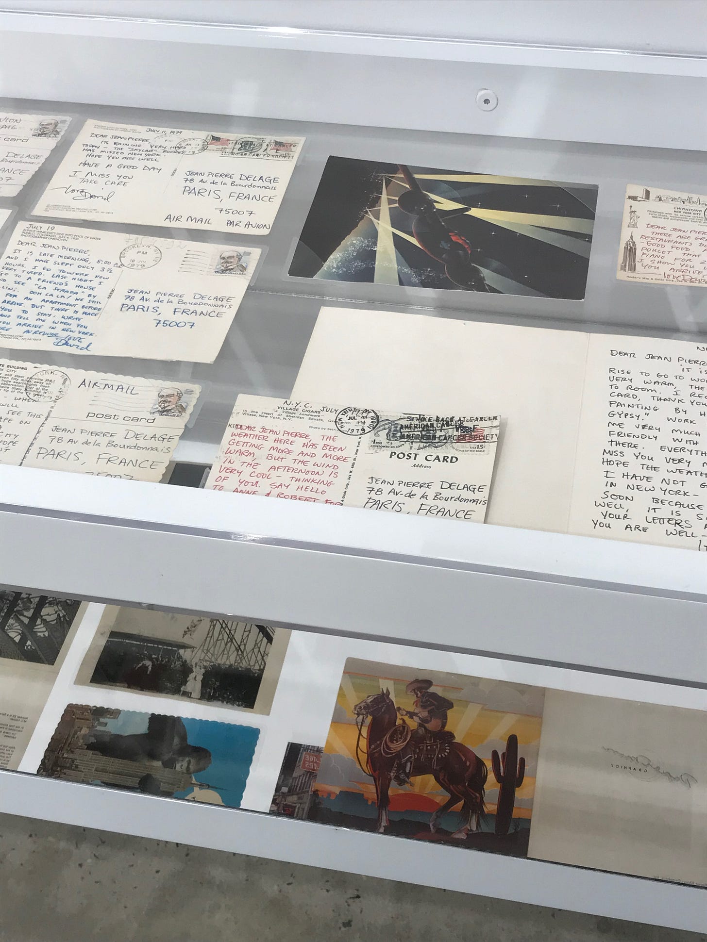 A vitrine filled with postcards written on in different coloured inks, red, black, blue, all addressed to Jean Pierre Delage from David Wojnarowicz