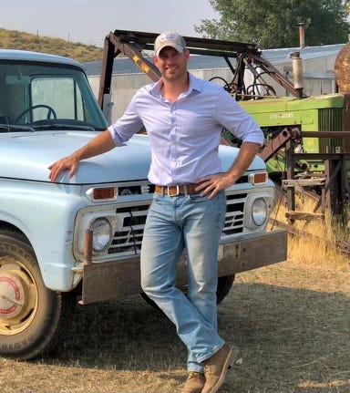 man in jeans and button down leans against a truck