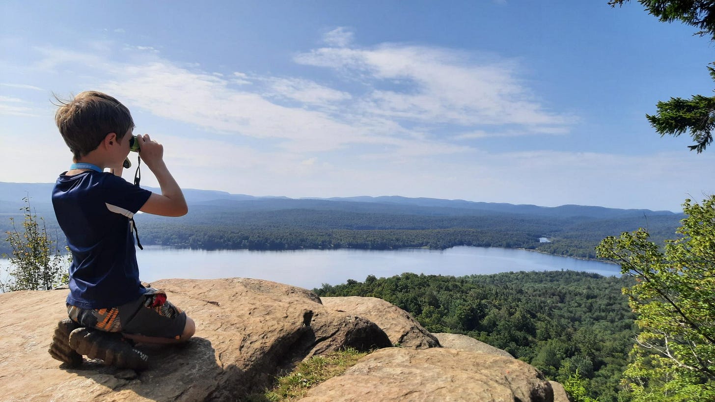A child looks through binoculars over Piseco Lake from Echo Cliffs