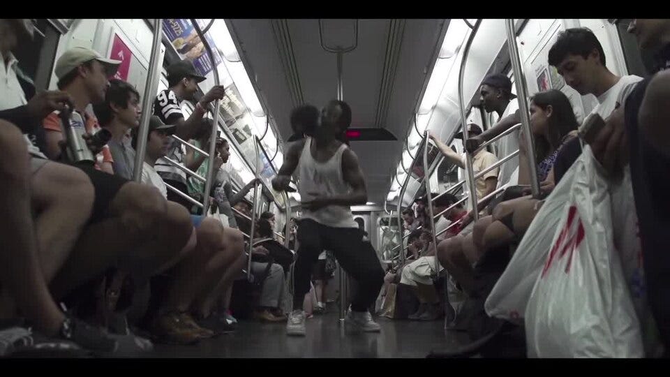 A dancer performs in the aisle of a New York City subway car while seated passengers watch. A dancer performs in the aisle of a New York City subway car while seated passengers watch.