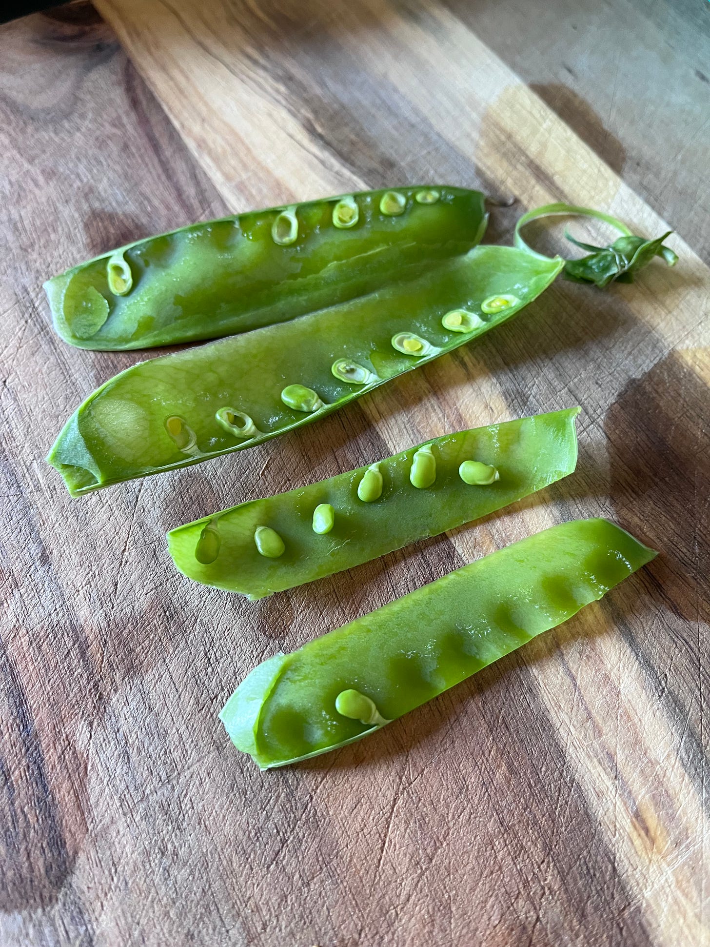 snow peas sitting on a wooden board, cut in half lengthways
