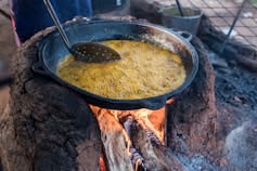 A pot balanced on large stones over a fire where bean cakes are frying in oil A pot balanced on large stones over a fire where bean cakes are frying in oil
