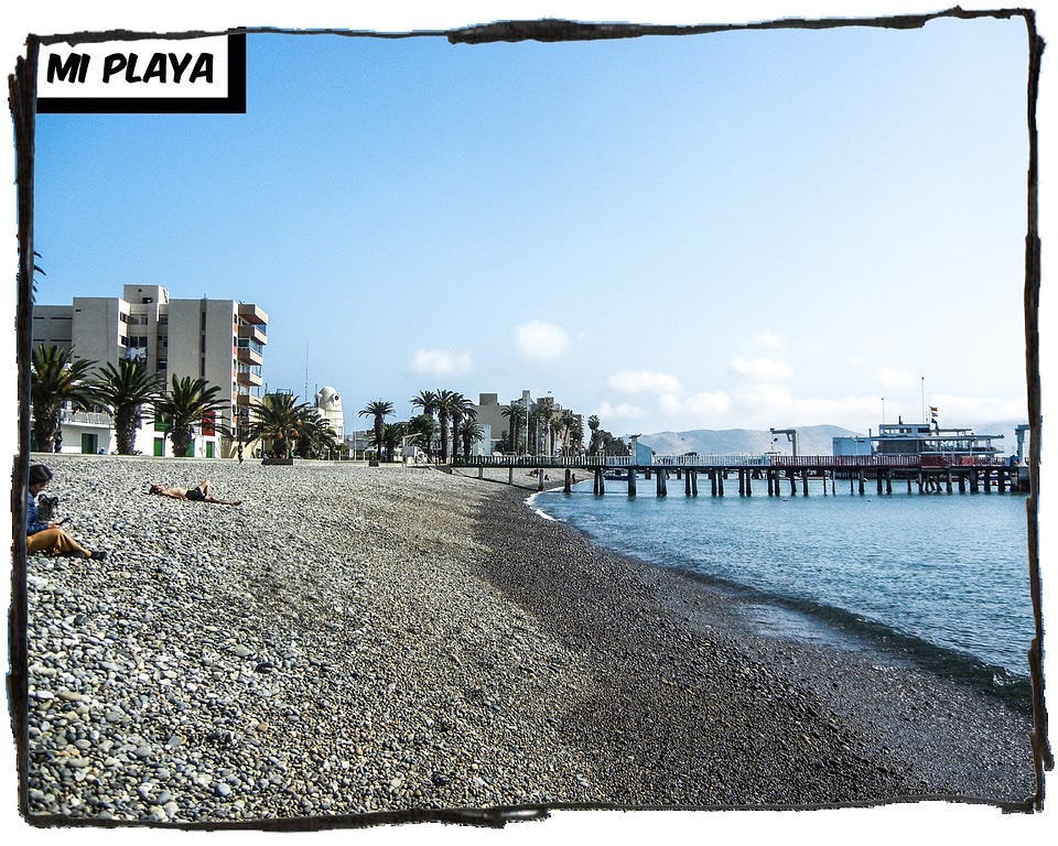 The beach with the stones at La Playa. There’s a pier in the middle of the image. The caption reads “Mi Playa.”