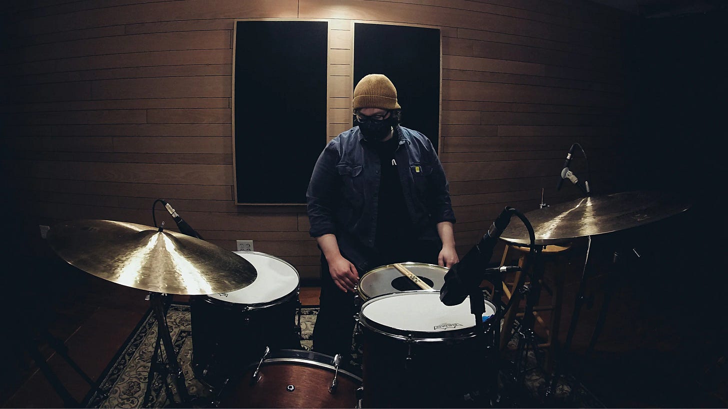 Andy in the studio with a red drum set, two big ride cymbals during COVID. 
