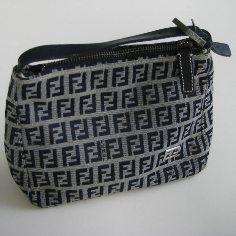 May include: A black and gray fabric handbag with a zipper closure and a silver Fendi logo. The bag is covered in a repeating pattern of black F's on a gray background.