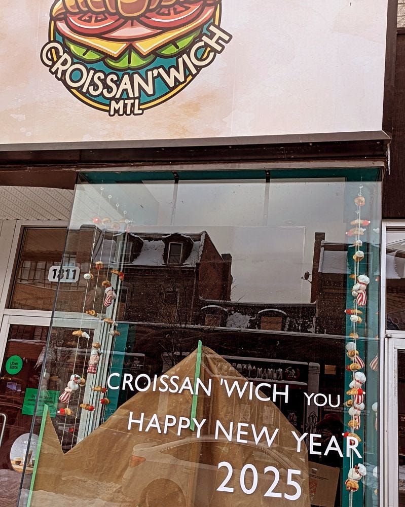 A sandwich shop named croissan'wich with a sign on the front glass window saying croissan'wich you happy new year 2025