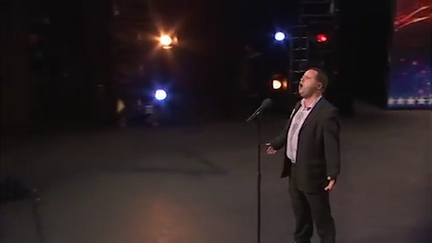 Paul Potts singing on the stage of Britain's Got Talent with arms outstretched 
