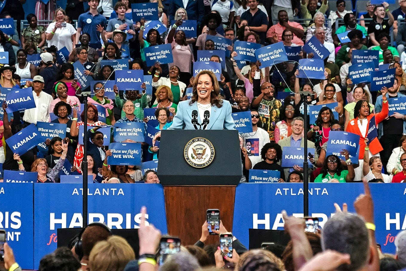 A woman stands at a lectern with an ecstatic crowd around her. A woman stands at a lectern with an ecstatic crowd around her.