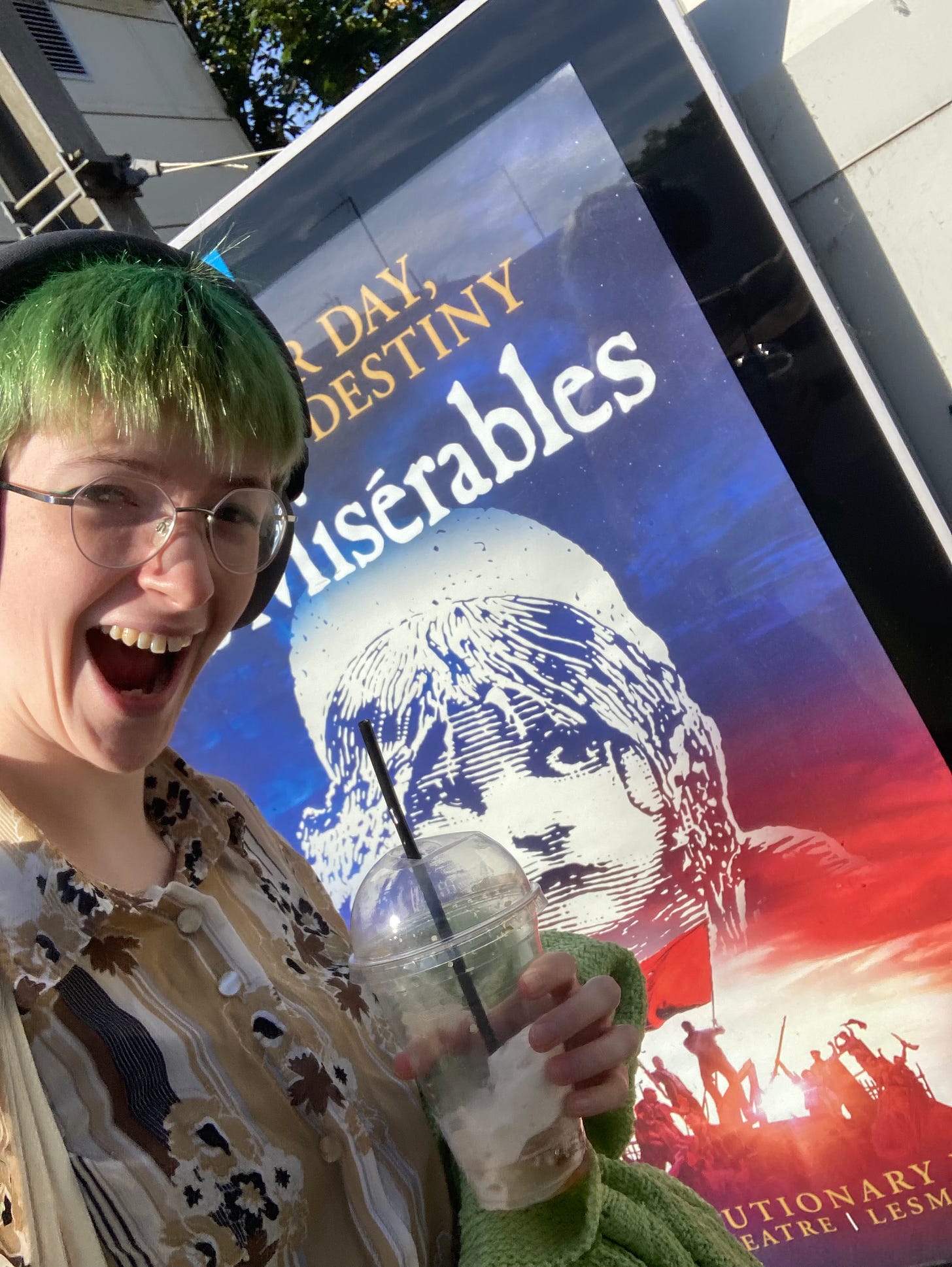 Selfie of me (green hair, yellow-brown stripy button-down shirt) next to a big Les Mis poster Selfie of me (green hair, yellow-brown stripy button-down shirt) next to a big Les Mis poster