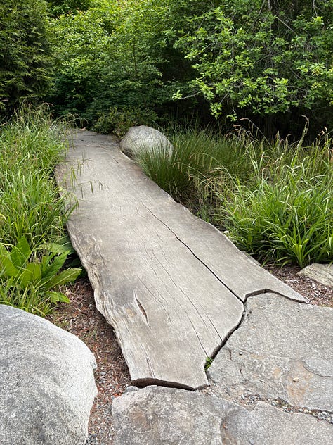 forest setting with labyrinth, brass prayer wheel, and bridge made from a tree
