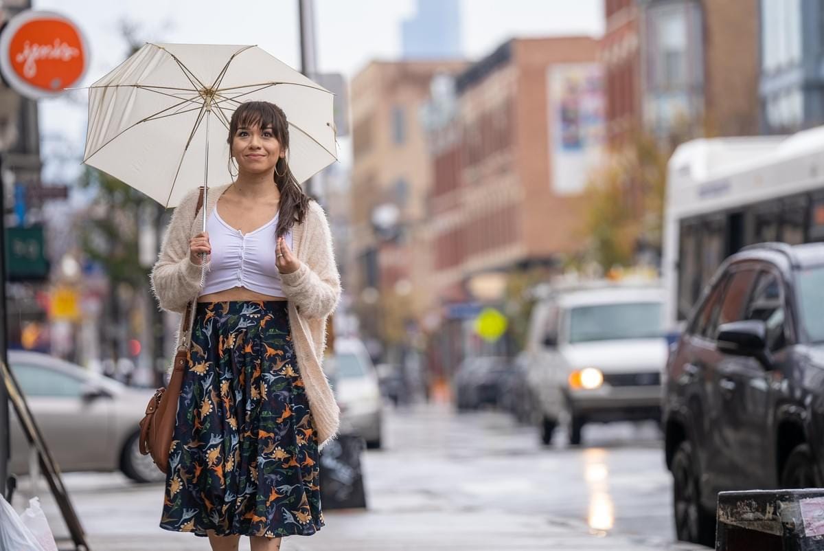 photo of a woman in a dinosaur skirt holding an open umbrella while standing by a street corner in new york city