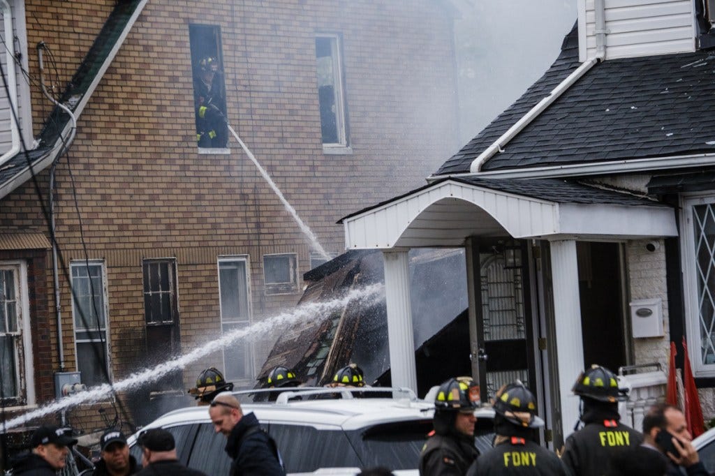 Firefighters battle a house fire in Queens, with one firefighter spraying water from an upper-story window.