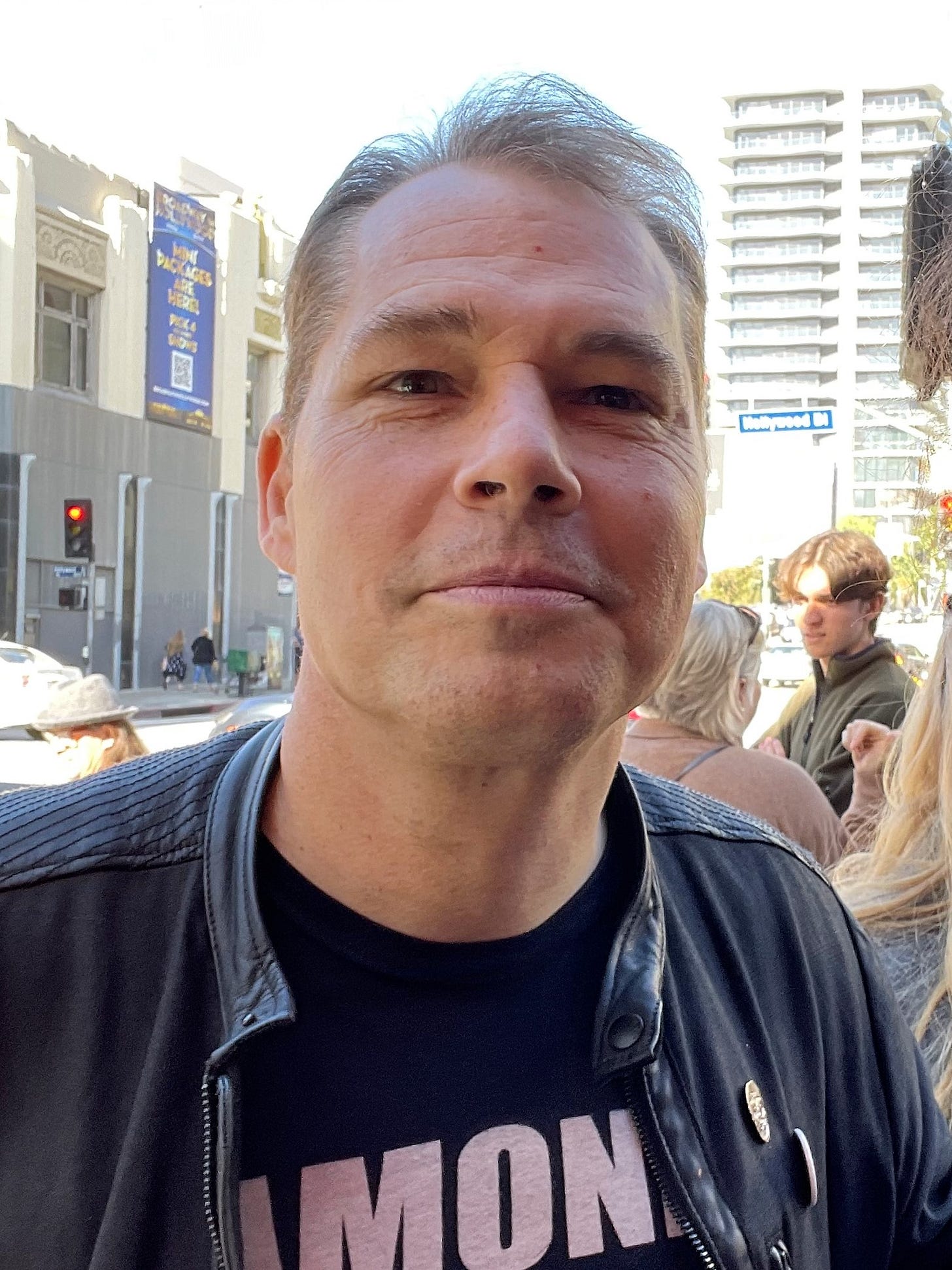 Shepard Fairey, grey hair swept back, in a black leather jacket on a Hollywood street.