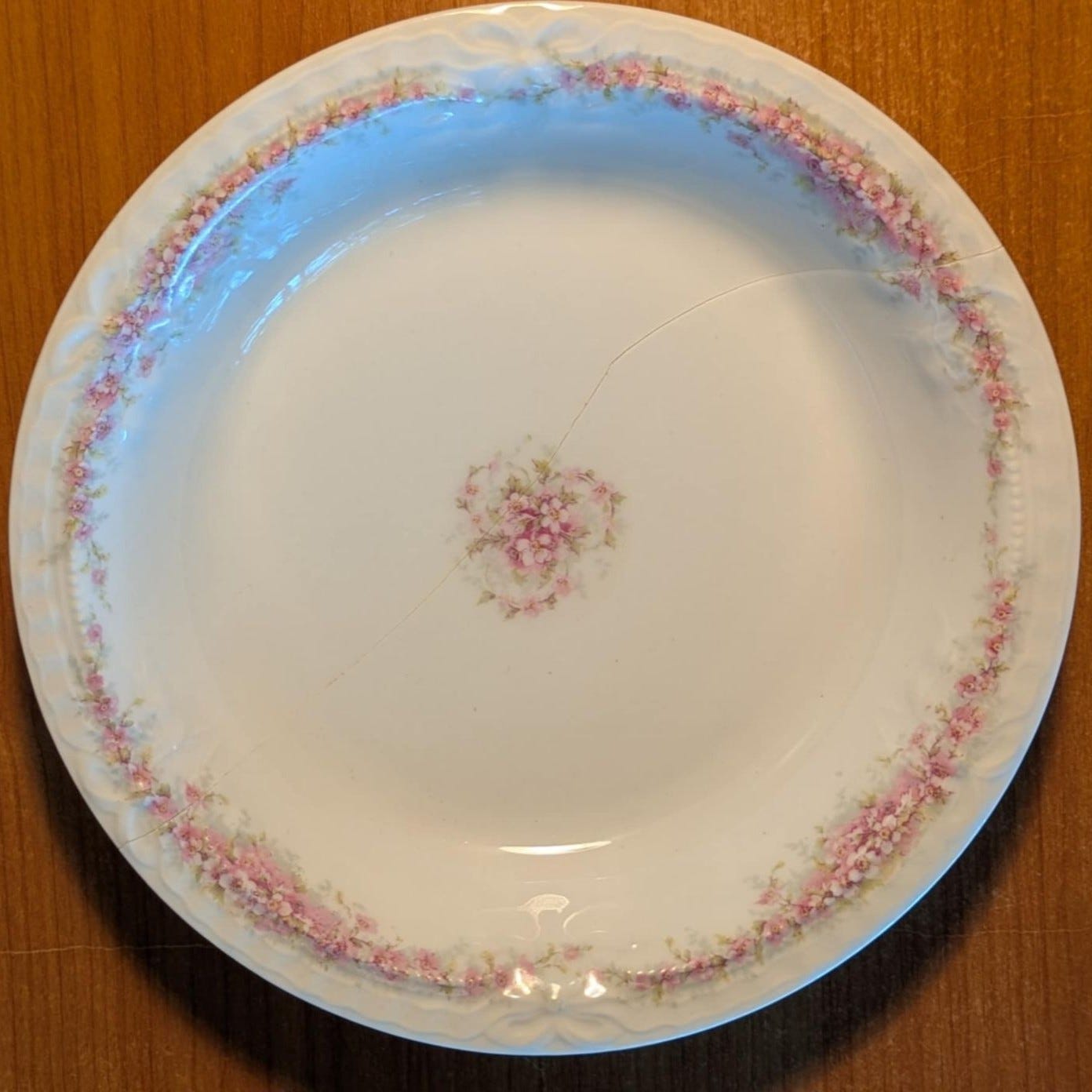 Close-up of a porcelain plate with delicate pink floral patterns around the edge and a mended crack.
