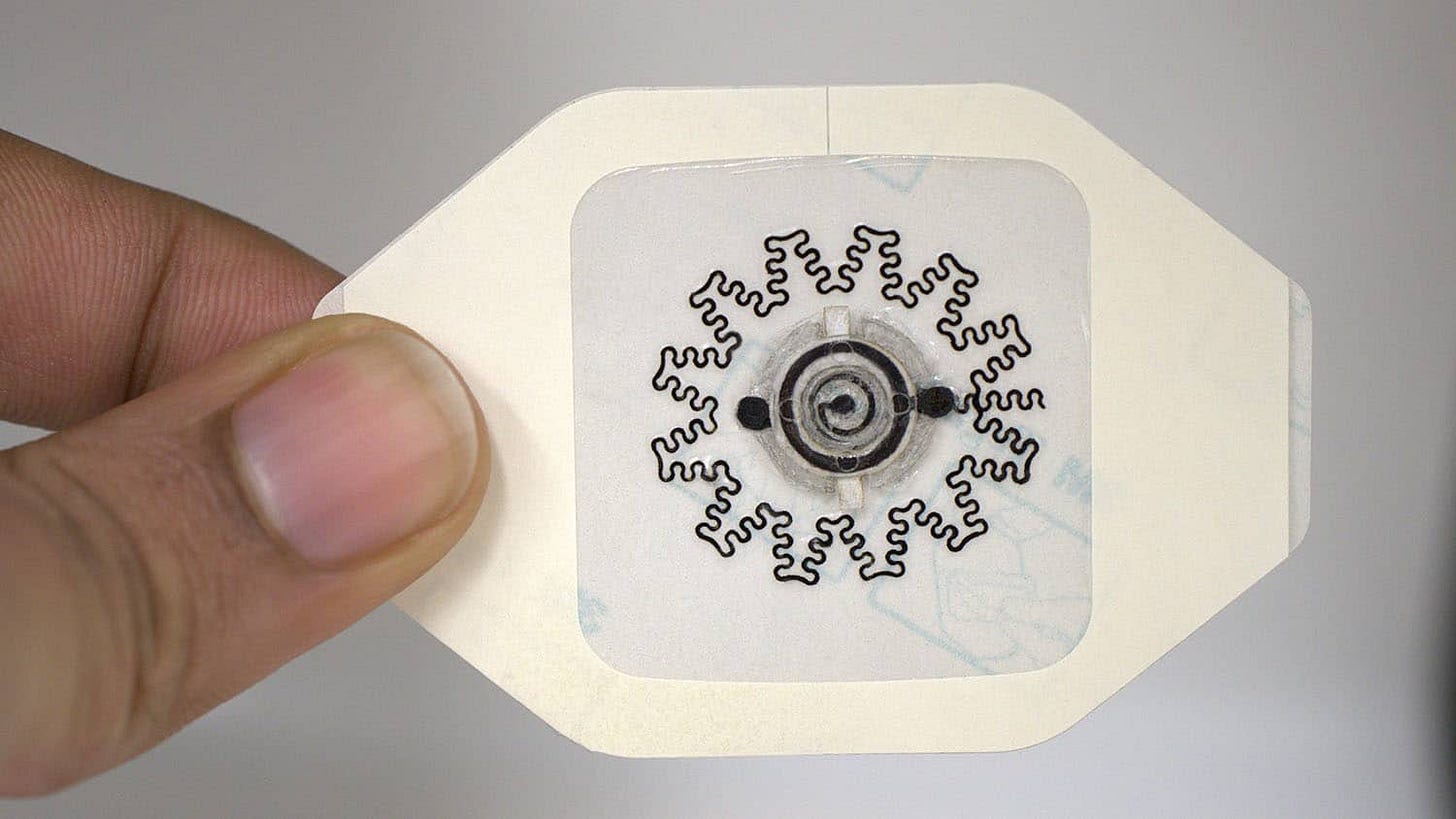 A hand holds a soft, flexible wearable device with a snowflake-like design on a white backing. A hand holds a soft, flexible wearable device with a snowflake-like design on a white backing.