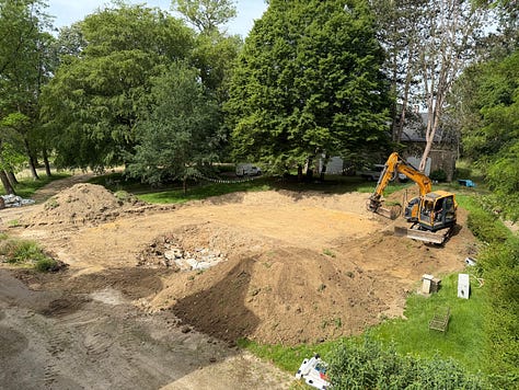 An excavator beside the château digs out the old swimming pool, with piles of earth in the foreground. The old pool half drained, its liner peeling away and green algae water pooled in the deep end. The cleared site where the old pool was, now bare earth and mounds of soil, with an excavator at the far end.
