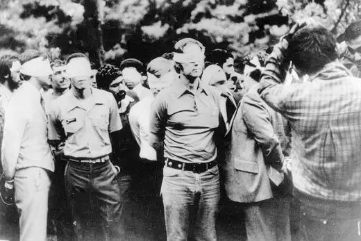 A group of American hostages in Iran stand blindfolded and handcuffed amid their captors.