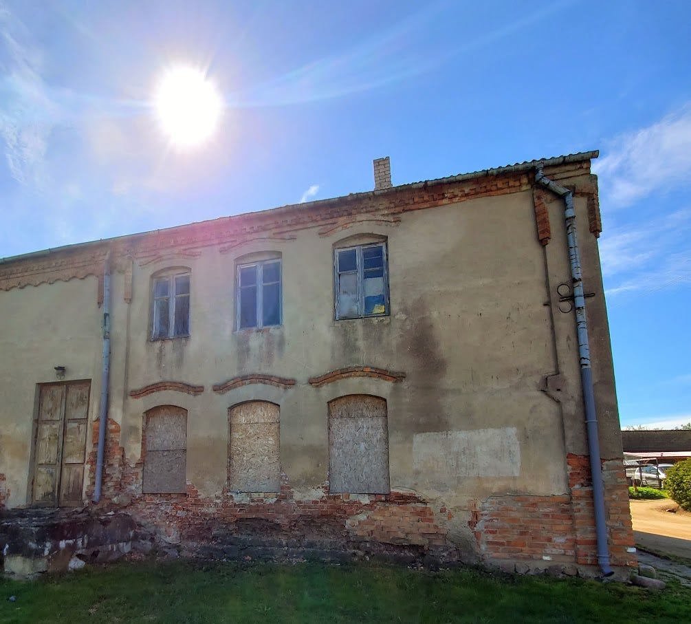 A brick and stucco building in disrepair under a bright blue sky with the sun shining overhead.