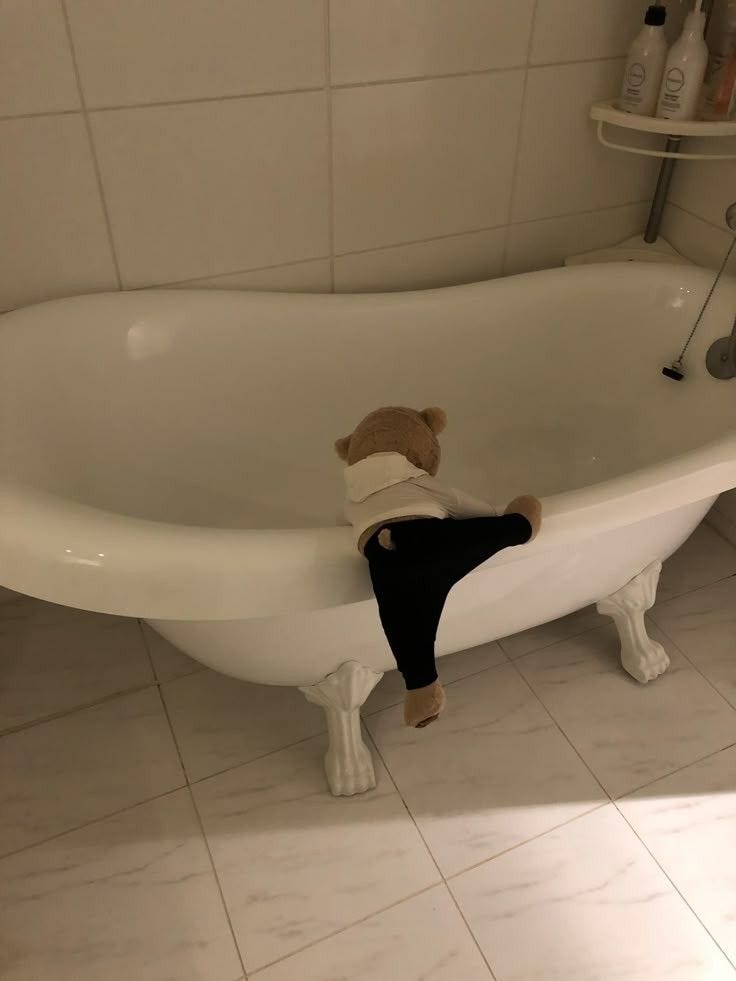 This may contain: a teddy bear sitting on the edge of a bathtub