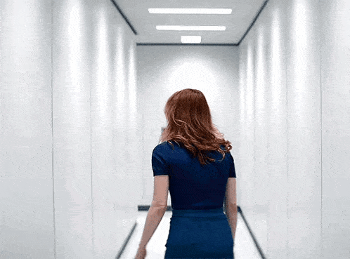 a woman in a blue dress is walking down a long hallway