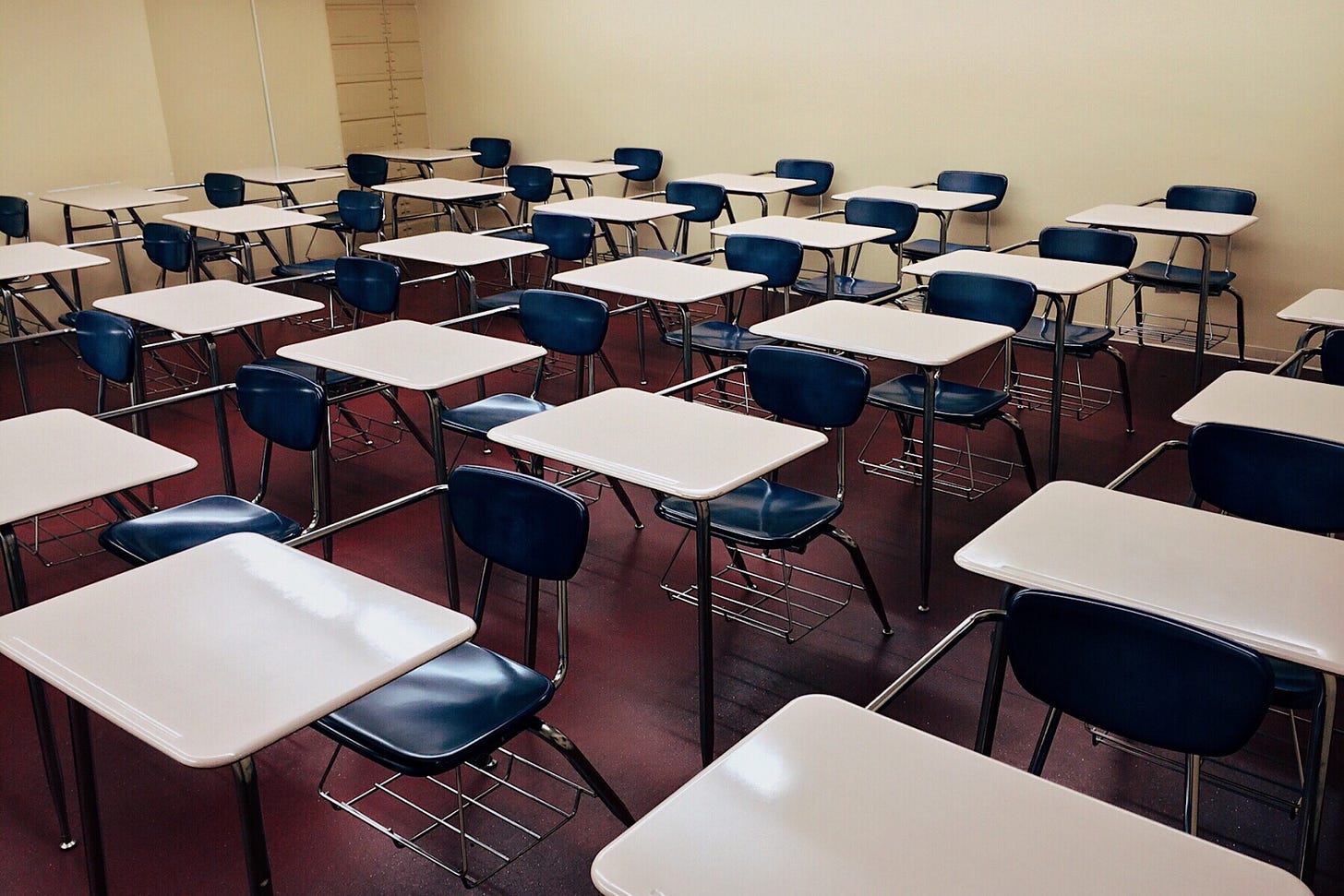6 rows of school desk chairs crammed into a room with tan walls no windows and red floors, it feels institutional 