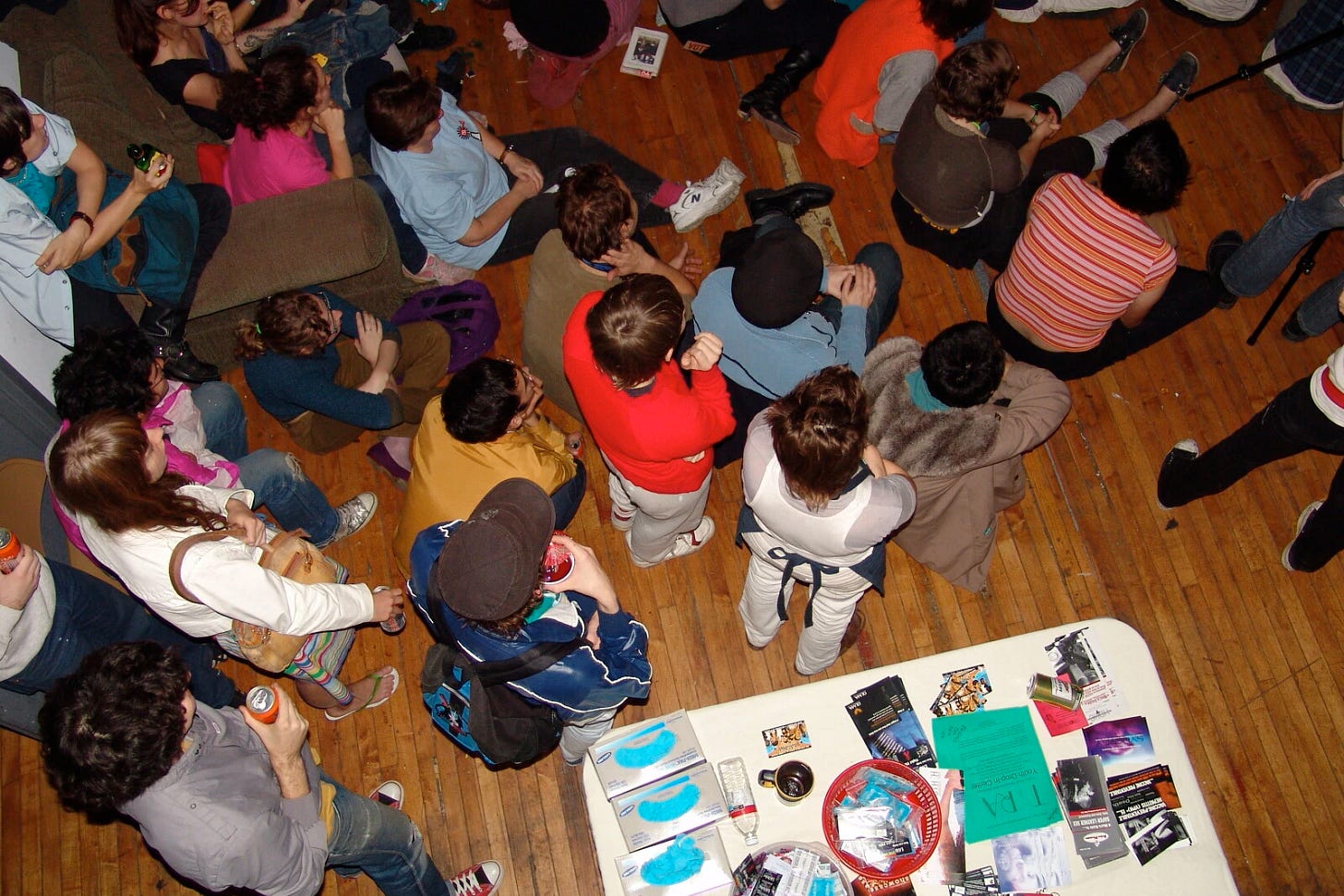 Overhead view of a group of people variously sitting or standing in a room looking at something out of view