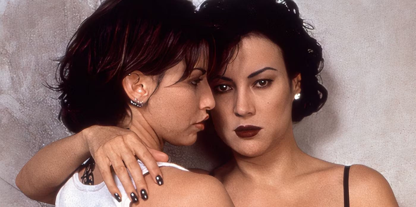 Gershon and Tilly hugging; Gershon in a wifebeater shirt; Tilley in a gown with straps; gershon's face in profile, Tilley looking at camera