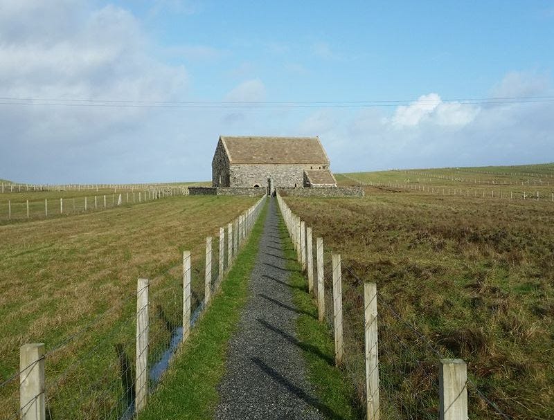 A narrow fenced path leads to a church in a sparse landscape