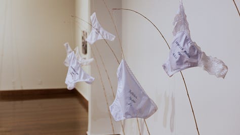 Instalação artística de Clara Salles traz calcinhas penduradas em varas de pescar, fixadas na areia no chão. Nas calcinhas, estão bordadas transcrições de juras de amor e textos que testemunham encontros amorosos explosivos.