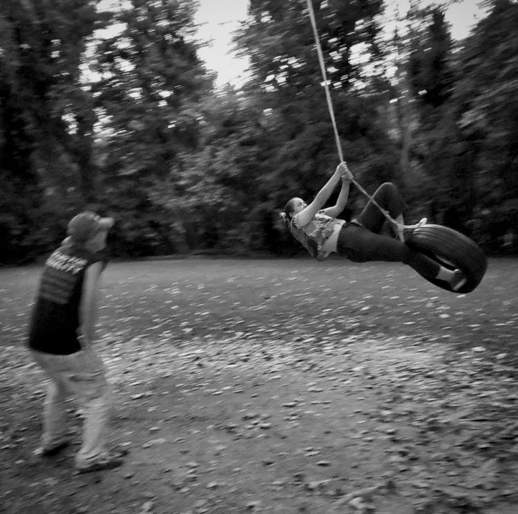 Photo by Annalisa Hartlaub - Person standing do the left, knees bent looking at another person swinging / hanging on a tire swing. Black and white film photo Photo by Annalisa Hartlaub - Person standing do the left, knees bent looking at another person swinging / hanging on a tire swing. Black and white film photo