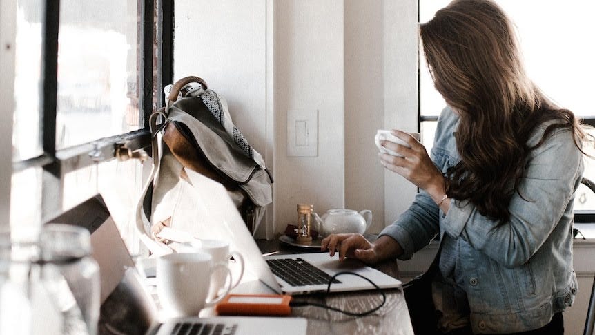 A woman sits at a computer with her hair shielding her face, drinking a coffee. A woman sits at a computer with her hair shielding her face, drinking a coffee.