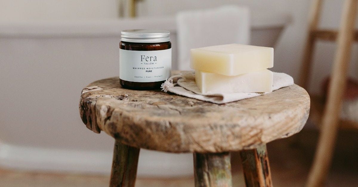 A jar of Pure Whipped Tallow on a rustic wooden stool with a home setting in the background