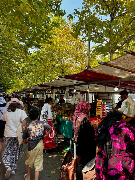 Photo 1 (busy market): Bustling outdoor farmers market under tree canopy with vendors in striped awnings and shoppers browsing produce Photo 2 (receipt): Hand holding a receipt showing 6 euros from a Paris market with bags of fresh produce visible in background Photo 3 (produce display): Colorful vegetable display at market stall featuring eggplants, cucumbers, celery, and ginger in wooden crates