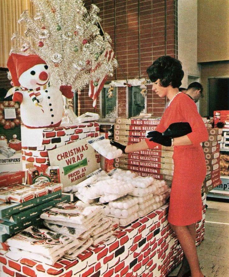 This may contain: a woman in an orange dress standing next to a display of christmas items at a store