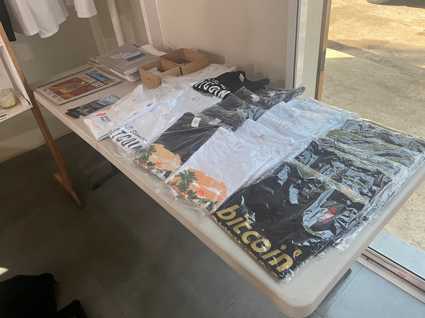 A table full of Bitcoin-themed t-shirts and pamphlets A table full of Bitcoin-themed t-shirts and pamphlets