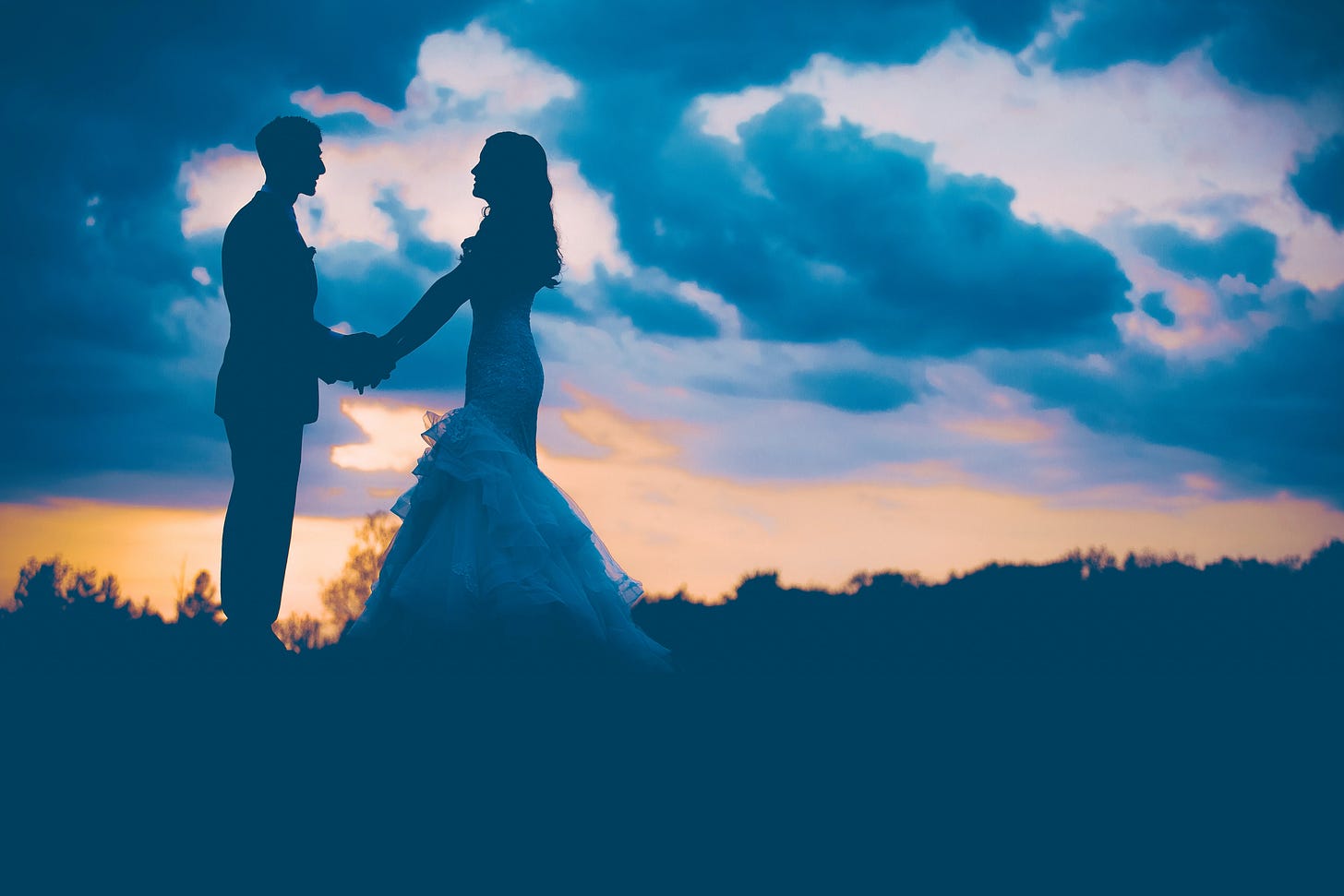 Silhouettes of a bride and groom standing face-to-face and holding hands against a dramatic, cloudy sky with deep blues and the glow of a sunset. The title "Soulmate Sorcery" appears in a white, handwritten-style script across the bottom of the image.