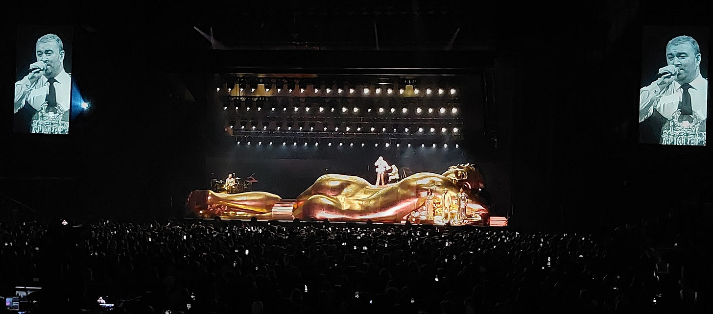 Sam Smith standing on a golden nude human form singing their heart out to a packed o2 arena