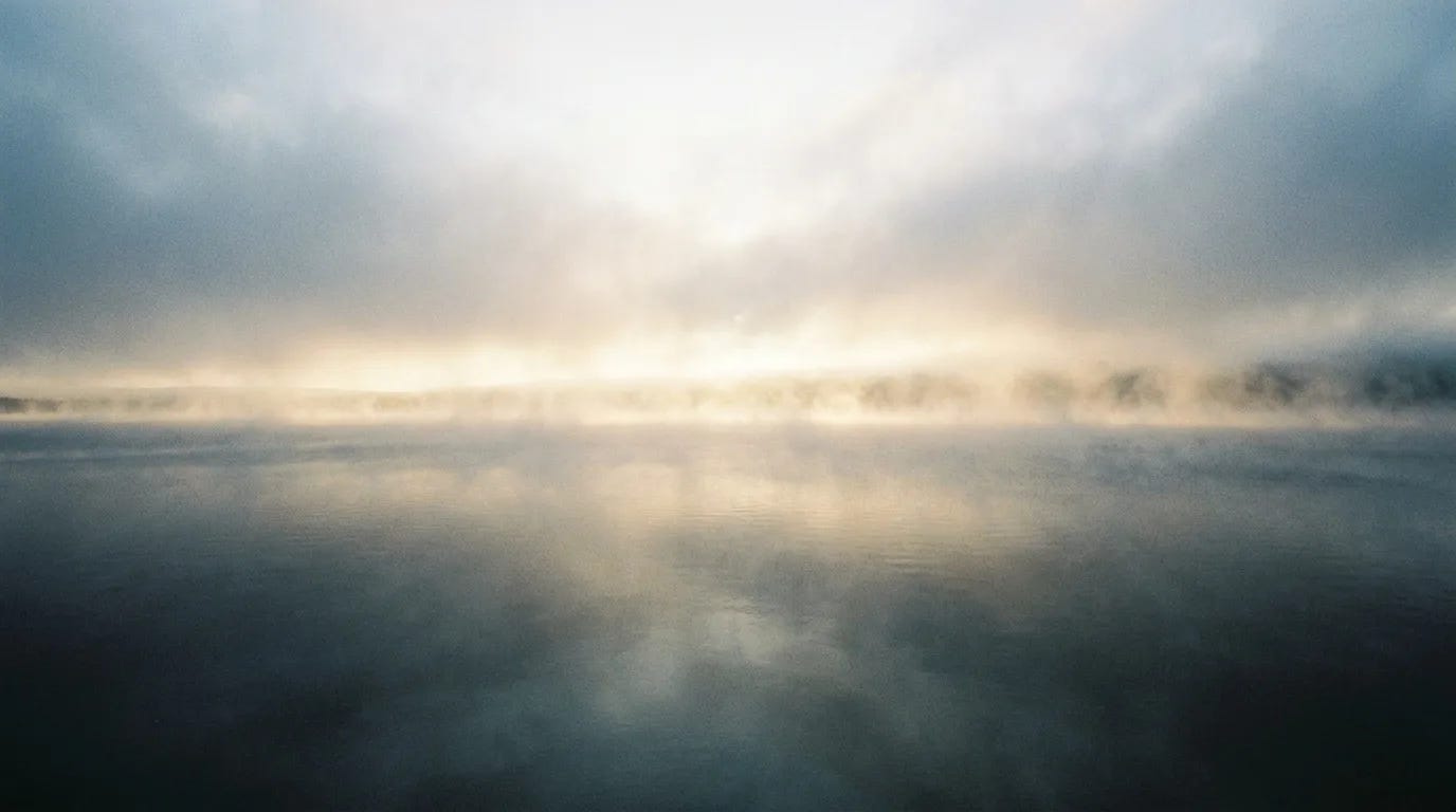 The first light of morning pouring across an empty landscape, mist lifting off dark water under a pale sky The first light of morning pouring across an empty landscape, mist lifting off dark water under a pale sky