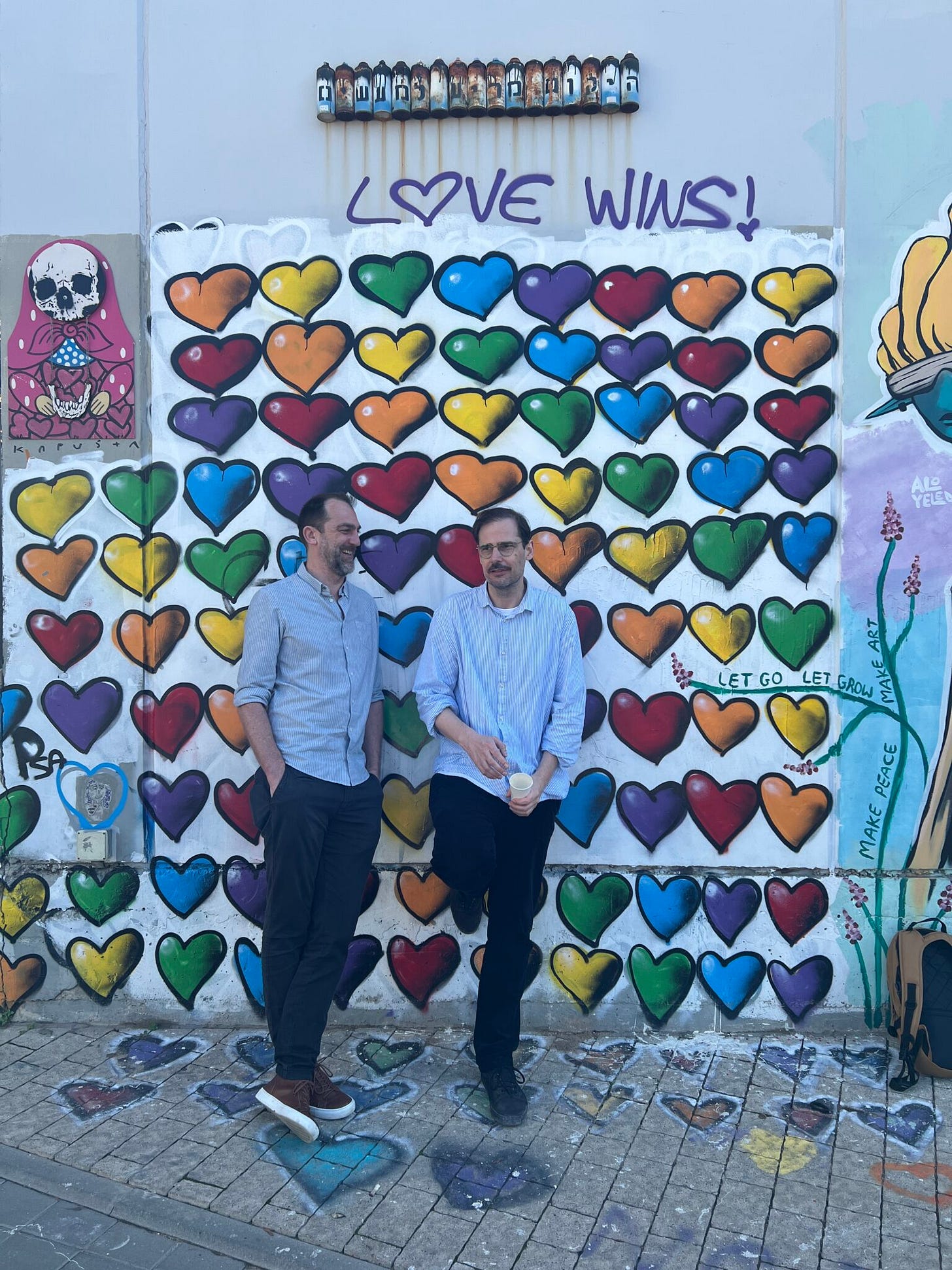 Street Art, viele bunte Herzen, „Love wins“, Michael und Jochen stehenm davor Street Art, viele bunte Herzen, „Love wins“, Michael und Jochen stehenm davor