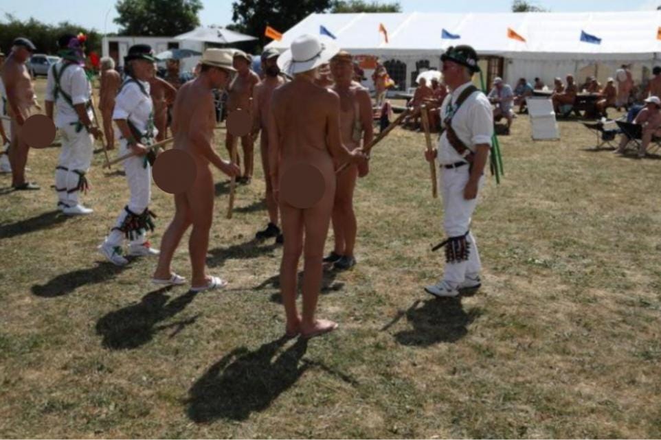 Naked festivalgoers with hats and props gather on a grassy field at Nudefest, engaging with traditionally dressed Morris dancers in front of a large white event tent. Naked festivalgoers with hats and props gather on a grassy field at Nudefest, engaging with traditionally dressed Morris dancers in front of a large white event tent.