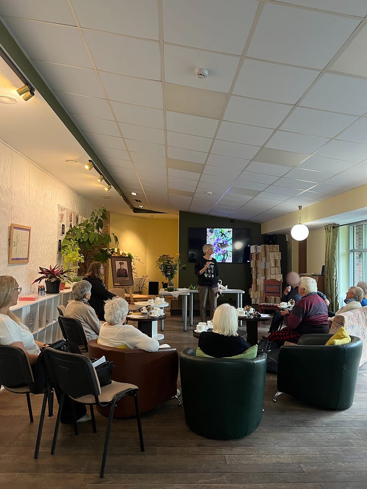 There are three images on the top, and two below. 1.	Activity workshop space inspired by the library’s natural environment and history. Photo by A. Petreike The environment was designed in reference to the library’s natural surroundings and historical background, reflecting the plant-themed concept of the workshop.  2.	Educational postcard with plant motif. Photo by A. Petreike Participant holding a plant-themed educational postcard, developed as part of the educational materials. The postcards invited participants to recognize familiar plants, color them and take them home to take home as a meaningful keepsake of the activity workshop. The back of the postcard featured the library contact person and their details, offering a way to connect.  3.	Educator interacting with participants. Photo by A. Petreike The educator engages participants by explaining and discussing different plants, fostering curiosity and sensory exploration (using a screen to show images, offering herbal tea to explore flavors, presenting postcards).  4.	Virtual reality experience. Photo by U. Padagiene Participant explores the library’s orangery using virtual reality glasses while the educator observes and guides the experience, enhancing engagement and sensory learning.  5.	Activity workshop session. Photo by A. Petreike