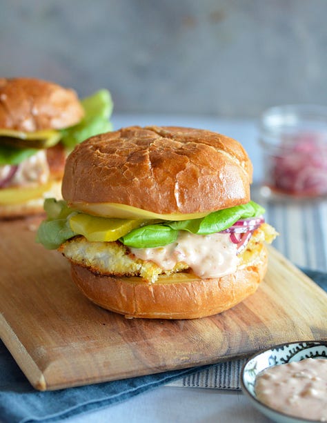 photos of fish almandine on a platter, seafood risotto in a white bowl, Karista pouring a seafood boil onto a plastic tablecloth, Karista holding a whole roasted fish, salmon with brown butter pasta with peas and mint and a crispy fish burger with special sauce sitting on a wooden board