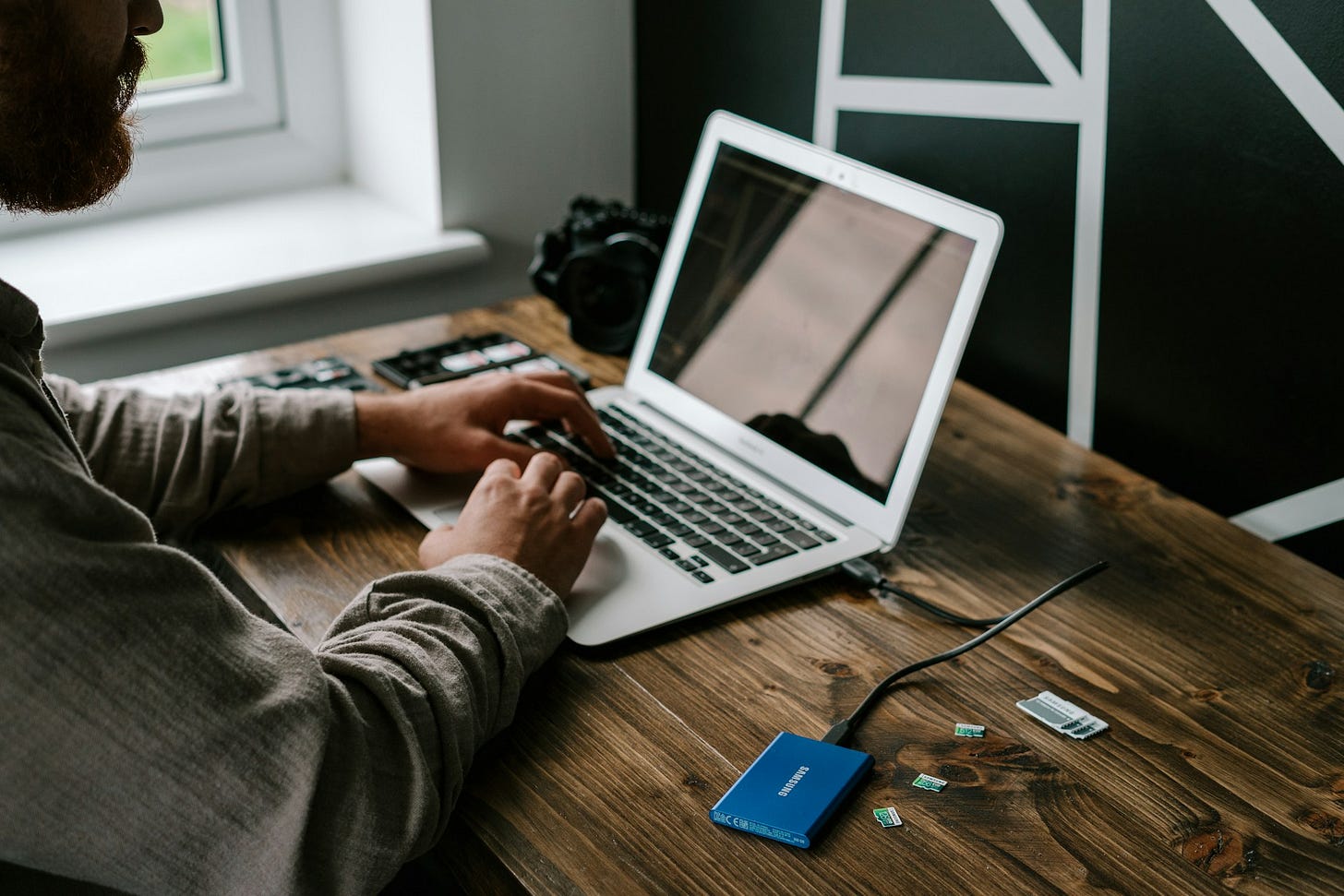 Mężczyzna pracujący na laptopie w home office. Do portu USB komputera podłączony jest zewnętrzny dysk twardy. Mężczyzna pracujący na laptopie w home office. Do portu USB komputera podłączony jest zewnętrzny dysk twardy.