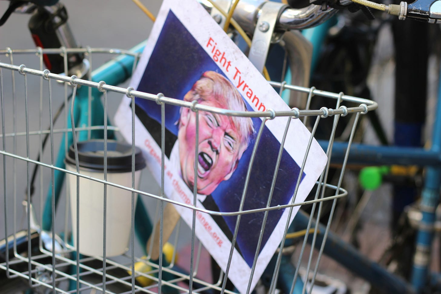A poster of Donald Trump with the words 'fight tyranny' on it sits in a bicycle basket beside a coffee cup. A poster of Donald Trump with the words 'fight tyranny' on it sits in a bicycle basket beside a coffee cup.